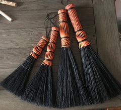 a collection of various sized hand made whisk brooms with woven handles made of orange dyed reed.